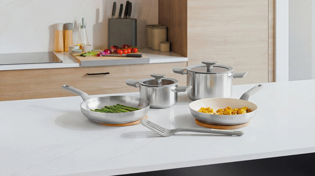 Stainless steel cookware set on a white countertop, including a casserole with lid, frying pan, and saucepans.